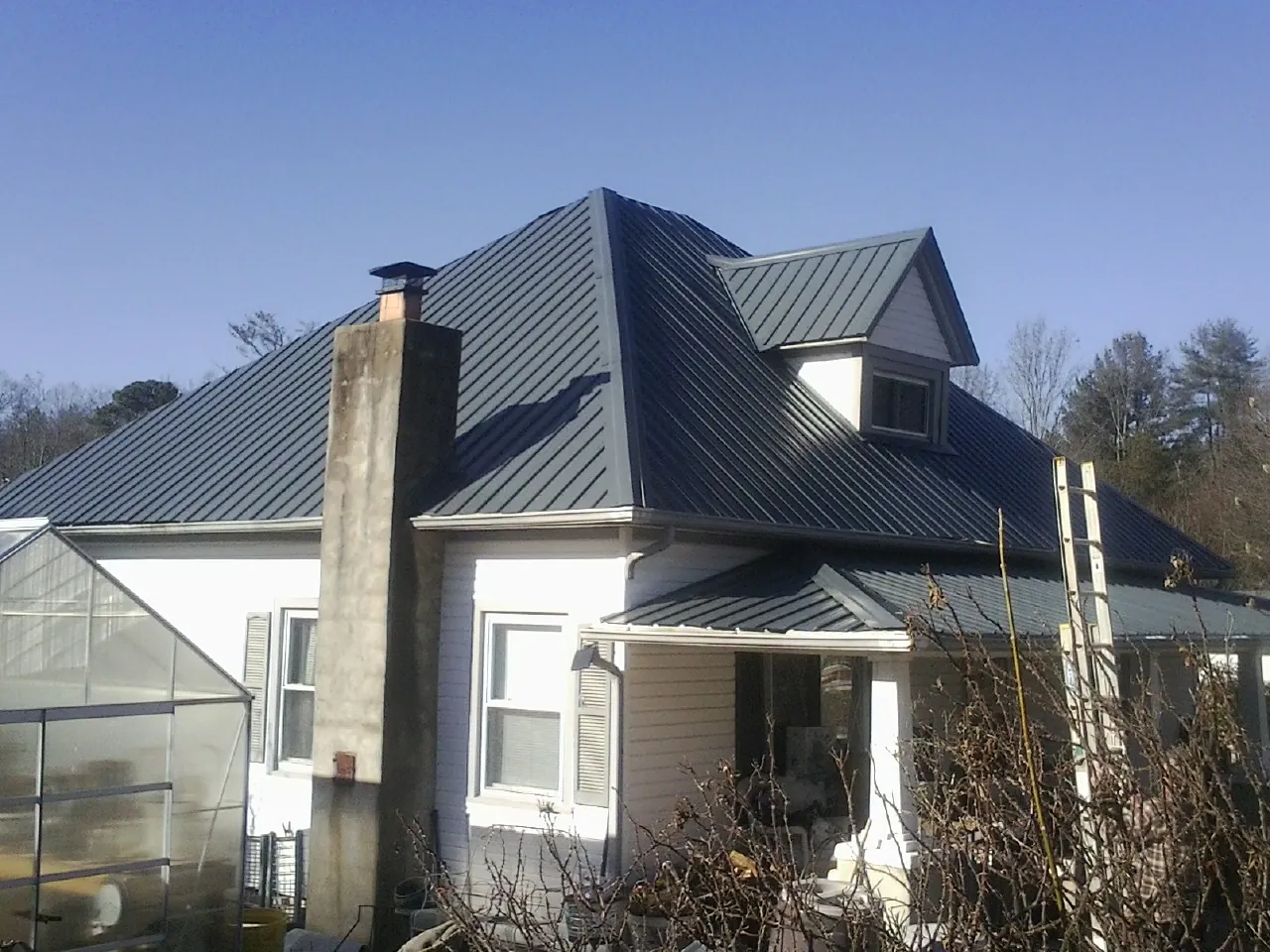 Dark blue standing seam metal roof on a white farmhouse with dormer — Slate & Tile Roof Repair by Roofing Brothers in Missouri City