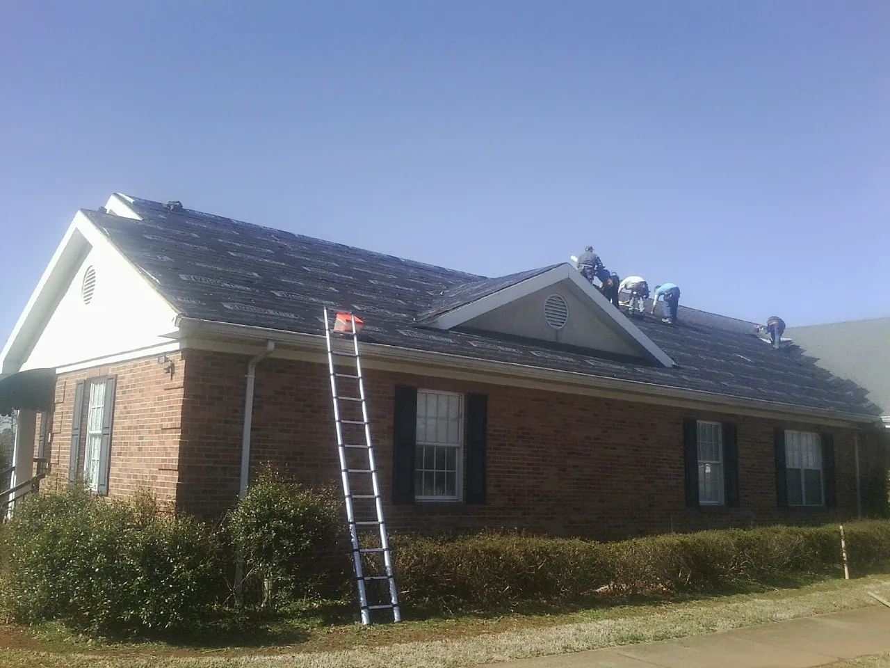 Crew tearing shingles off a brick ranch roof with a ladder set — Emergency Roof Repair work by our crew in Missouri City