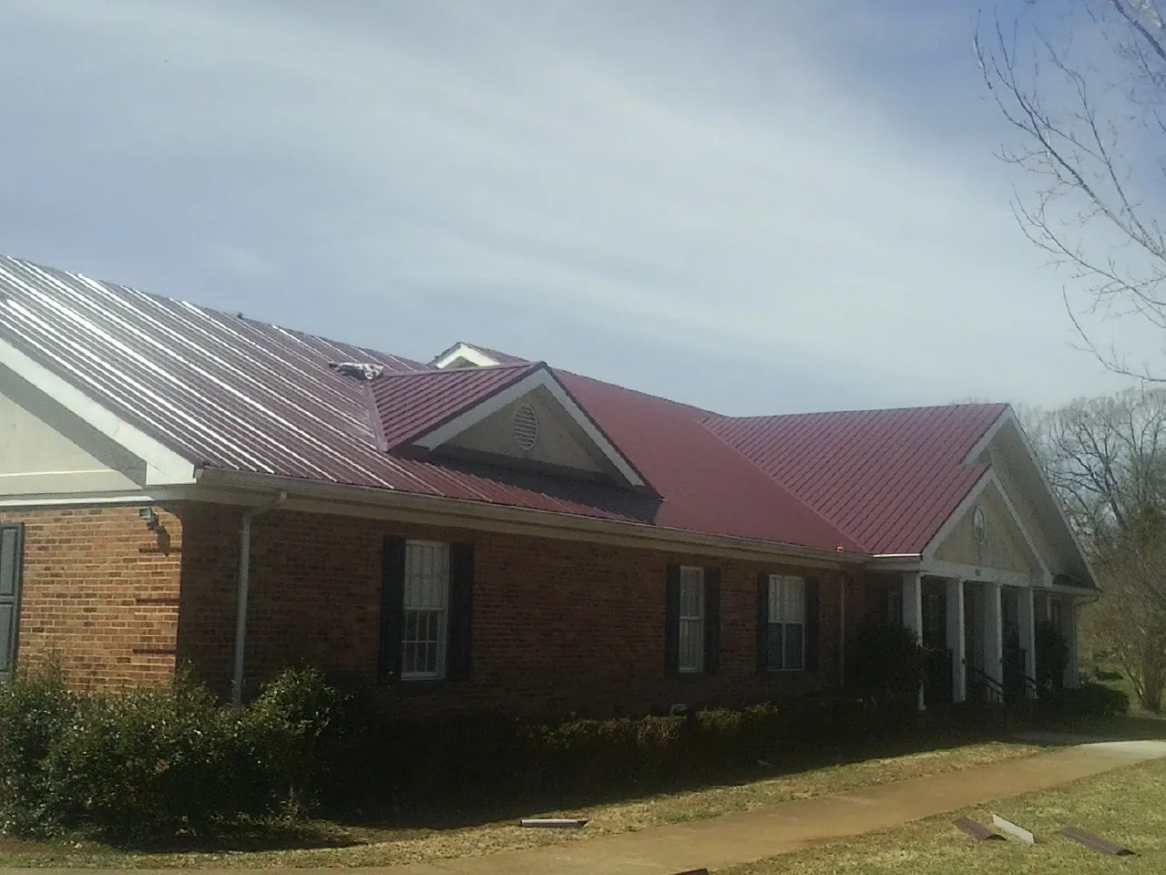 Red metal roof with gabled entries on a long brick building, from a Hail Damage Roof Repair job in Missouri City