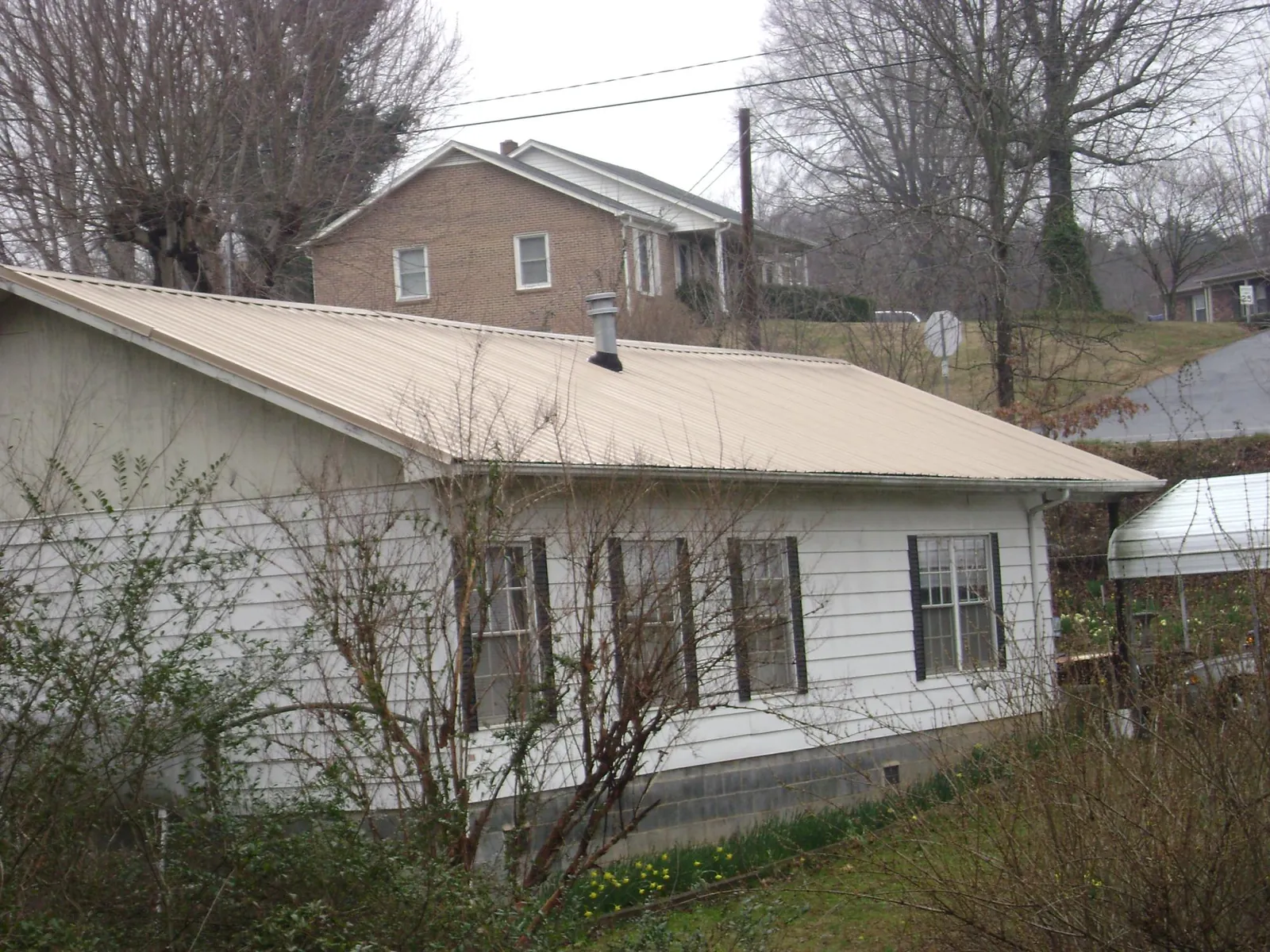 Tan metal roof on a white sided house set into a hillside — Commercial Roofing by Roofing Brothers in Missouri City
