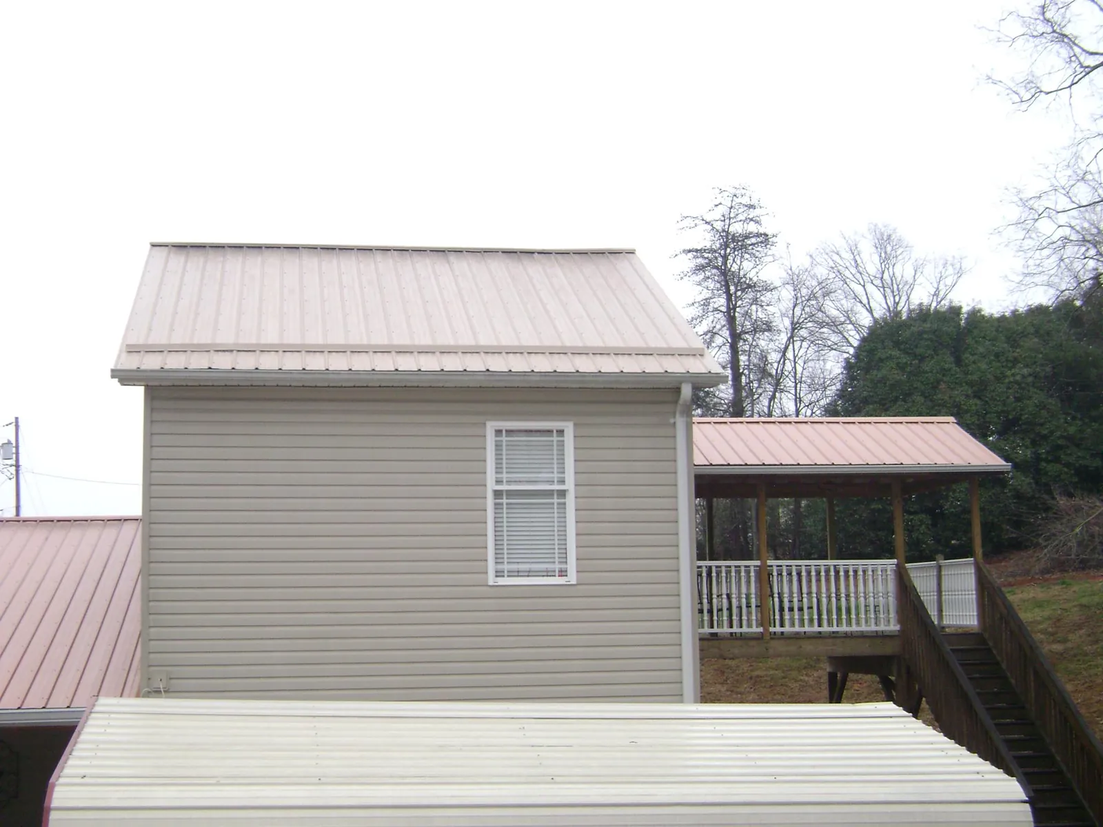 Tan metal roofs on a two story addition and attached porch, from a Roof Replacement job in Missouri City